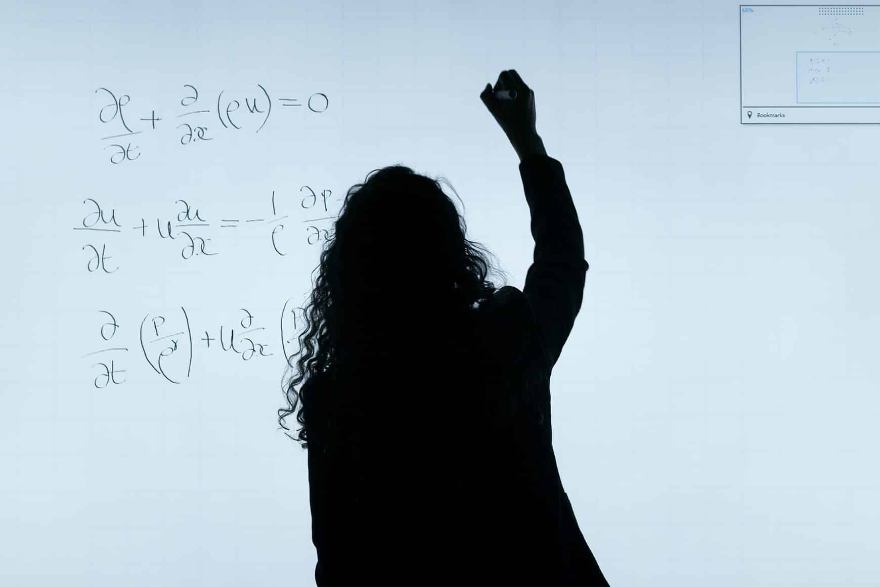 A silhouetted woman writing equations on a whiteboard